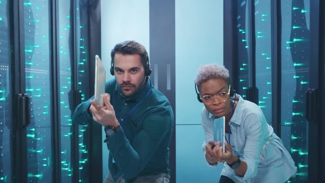 Professional multi-race armed spies on secret operation sneaking in server room walking aiming tablets like guns working in team. Data center. Fun concept.