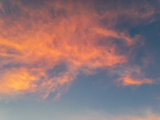 Clouds on a blue sky painted in the crimson light of the sun at sunset on an autumn evening.