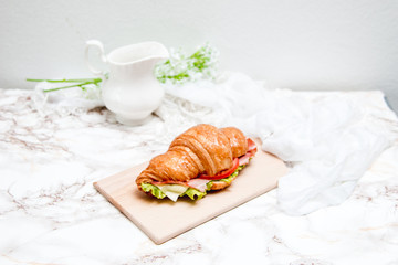 Sandwich croissant on a marble surface and wooden plate 