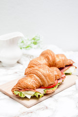 Sandwich croissant on a marble surface and wooden plate 