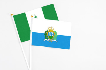 San Marino and Norfolk Island stick flags on white background. High quality fabric, miniature national flag. Peaceful global concept.White floor for copy space.