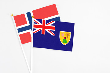 Fototapeta premium Turks And Caicos Islands and Norway stick flags on white background. High quality fabric, miniature national flag. Peaceful global concept.White floor for copy space.