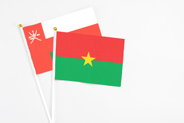 Burkina Faso and Oman stick flags on white background. High quality fabric, miniature national flag. Peaceful global concept.White floor for copy space.