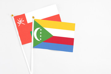 Comoros and Oman stick flags on white background. High quality fabric, miniature national flag. Peaceful global concept.White floor for copy space.