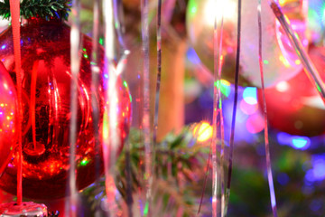 Red ball on Christmas tree. Blured holiday background with garland, glass toys, balls, lights. Colorful decoration close-up.