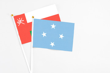 Micronesia and Oman stick flags on white background. High quality fabric, miniature national flag. Peaceful global concept.White floor for copy space.