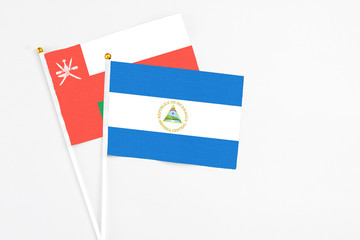 Nicaragua and Oman stick flags on white background. High quality fabric, miniature national flag. Peaceful global concept.White floor for copy space.