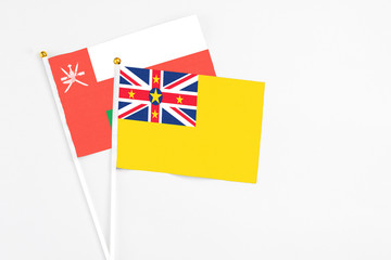Fototapeta premium Niue and Oman stick flags on white background. High quality fabric, miniature national flag. Peaceful global concept.White floor for copy space.