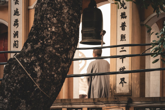 A buddist monk rings a bell during a bright sunrise in Hanoi, Capital of Vietnam wearing a white robe surrounded by Asian text