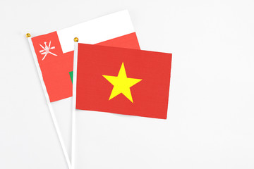 Vietnam and Oman stick flags on white background. High quality fabric, miniature national flag. Peaceful global concept.White floor for copy space.