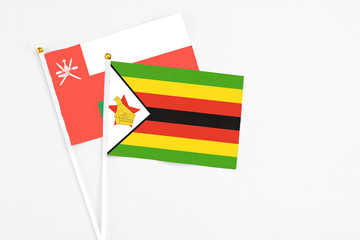 Zimbabwe and Oman stick flags on white background. High quality fabric, miniature national flag. Peaceful global concept.White floor for copy space.