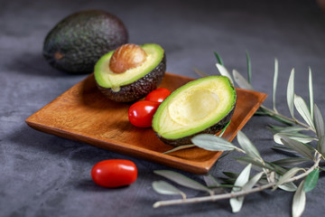 Fresh ripe avocado and some little tomatoes cherry on the wooden plate and on the dark background.