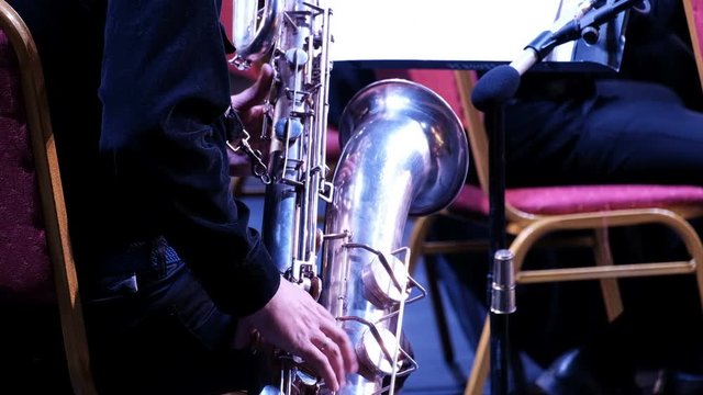 A man's hand in a black suit on a saxophone in a jazz band. Back view. Close-up. Musician of a brass band. Festive concert of the symphony orchestra.