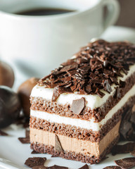 Cake of chocolate and cream with a cup of coffee on the white saucer closeup, macro.