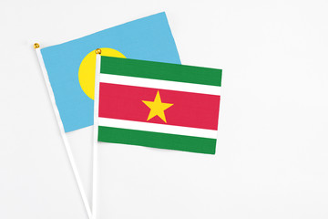 Suriname and Palau stick flags on white background. High quality fabric, miniature national flag. Peaceful global concept.White floor for copy space.