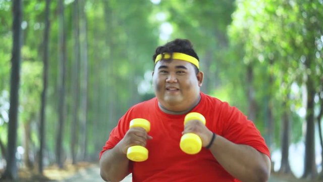 Slow motion of happy obese man exercising with dumbbells while punching on the camera at the park