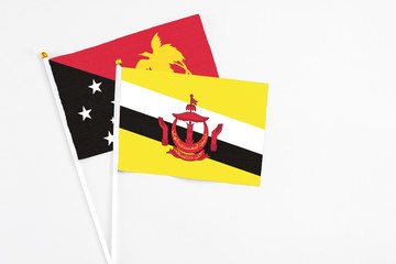 Brunei and Papua New Guinea stick flags on white background. High quality fabric, miniature national flag. Peaceful global concept.White floor for copy space.