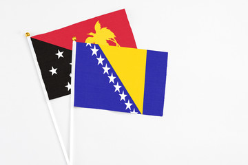 Bosnia Herzegovina and Papua New Guinea stick flags on white background. High quality fabric, miniature national flag. Peaceful global concept.White floor for copy space.