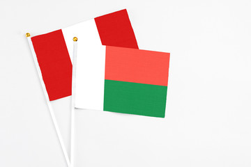 Madagascar and Peru stick flags on white background. High quality fabric, miniature national flag. Peaceful global concept.White floor for copy space.