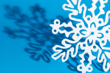 Fototapeta na wymiar Holiday background of sparkly white snowflake ornaments casting shadow on a bright blue winter background
