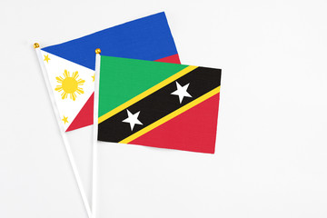 Obraz premium Saint Kitts And Nevis and Philippines stick flags on white background. High quality fabric, miniature national flag. Peaceful global concept.White floor for copy space.