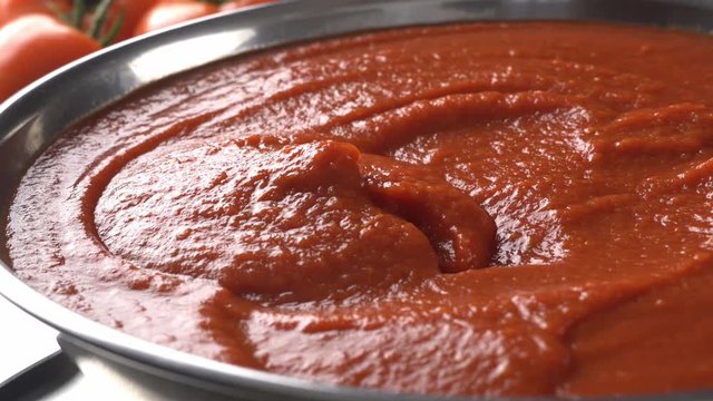 Spoon scooping freshly made tomato sauce from a stainless steel bowl.
