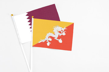 Bhutan and Qatar stick flags on white background. High quality fabric, miniature national flag. Peaceful global concept.White floor for copy space.