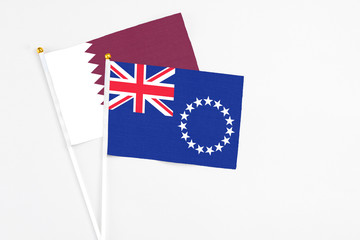 Fototapeta premium Cook Islands and Qatar stick flags on white background. High quality fabric, miniature national flag. Peaceful global concept.White floor for copy space.