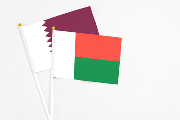 Madagascar and Qatar stick flags on white background. High quality fabric, miniature national flag. Peaceful global concept.White floor for copy space.