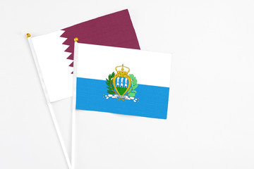 San Marino and Qatar stick flags on white background. High quality fabric, miniature national flag. Peaceful global concept.White floor for copy space.