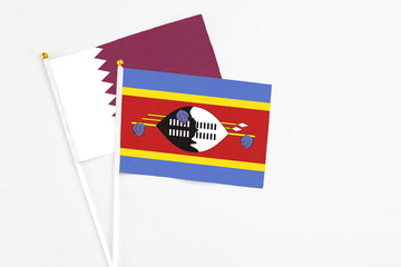 Swaziland and Qatar stick flags on white background. High quality fabric, miniature national flag. Peaceful global concept.White floor for copy space.