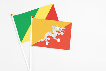 Bhutan and Republic Of The Congo stick flags on white background. High quality fabric, miniature national flag. Peaceful global concept.White floor for copy space.