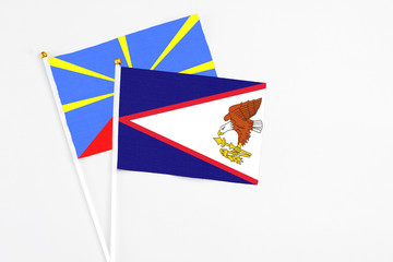 American Samoa and Reunion stick flags on white background. High quality fabric, miniature national flag. Peaceful global concept.White floor for copy space.