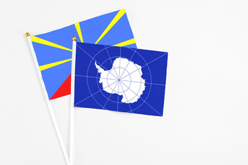 Antarctica and Reunion stick flags on white background. High quality fabric, miniature national flag. Peaceful global concept.White floor for copy space.