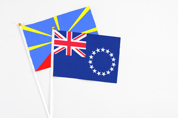 Fototapeta premium Cook Islands and Reunion stick flags on white background. High quality fabric, miniature national flag. Peaceful global concept.White floor for copy space.