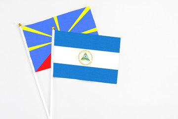 Nicaragua and Reunion stick flags on white background. High quality fabric, miniature national flag. Peaceful global concept.White floor for copy space.