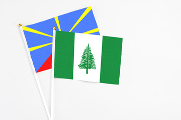 Norfolk Island and Reunion stick flags on white background. High quality fabric, miniature national flag. Peaceful global concept.White floor for copy space.