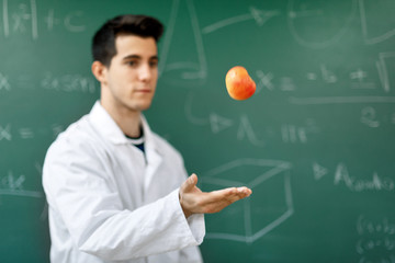 Smiling student with white coat throwing an apple up, on green chalkboard with equations background...