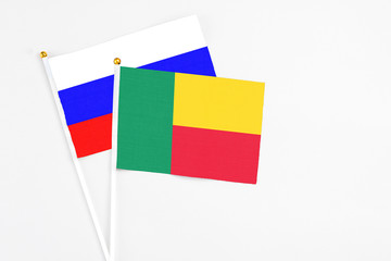 Benin and Russia stick flags on white background. High quality fabric, miniature national flag. Peaceful global concept.White floor for copy space.