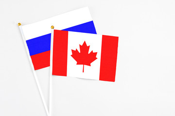 Canada and Russia stick flags on white background. High quality fabric, miniature national flag. Peaceful global concept.White floor for copy space.