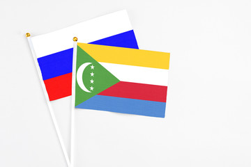 Comoros and Russia stick flags on white background. High quality fabric, miniature national flag. Peaceful global concept.White floor for copy space.
