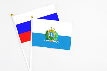 San Marino and Russia stick flags on white background. High quality fabric, miniature national flag. Peaceful global concept.White floor for copy space.