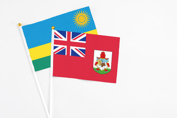 Fototapeta premium Bermuda and Rwanda stick flags on white background. High quality fabric, miniature national flag. Peaceful global concept.White floor for copy space.