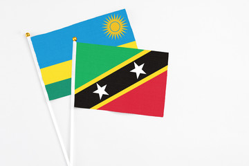Saint Kitts And Nevis and Rwanda stick flags on white background. High quality fabric, miniature national flag. Peaceful global concept.White floor for copy space.