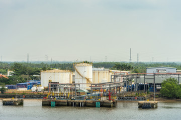 Long Tau River, Vietnam - March 12, 2019: Phuoc Khanh area. PetroVietnam in and out pumping installation where ships are handled. White tanks and green foliage in back under light blue sky.