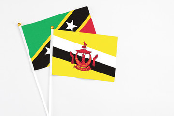 Brunei and Saint Kitts And Nevis stick flags on white background. High quality fabric, miniature national flag. Peaceful global concept.White floor for copy space.