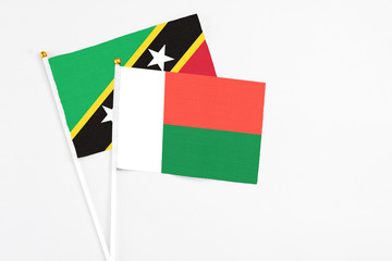 Madagascar and Saint Kitts And Nevis stick flags on white background. High quality fabric, miniature national flag. Peaceful global concept.White floor for copy space.