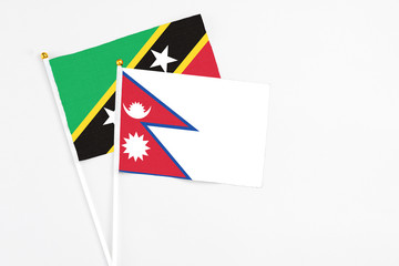 Nepal and Saint Kitts And Nevis stick flags on white background. High quality fabric, miniature national flag. Peaceful global concept.White floor for copy space.