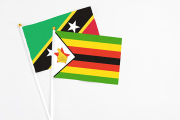 Zimbabwe and Saint Kitts And Nevis stick flags on white background. High quality fabric, miniature national flag. Peaceful global concept.White floor for copy space.