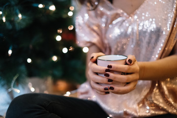 Woman's hands holding cup next to Christmas tree